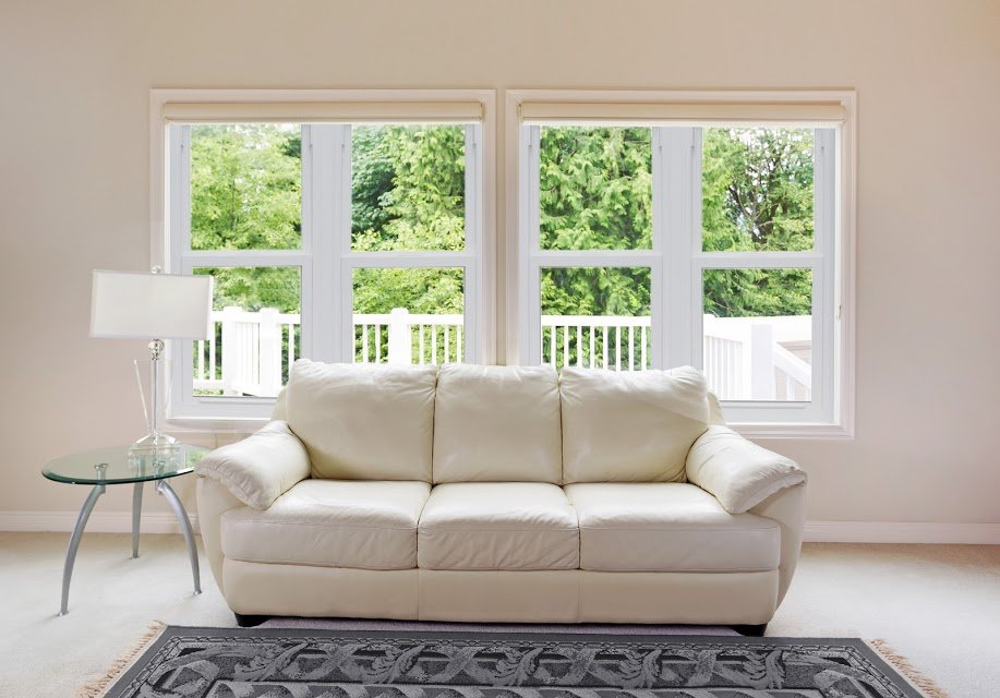 Clean family room with white leather couch and large windows showing bright green trees in background.